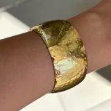 Brazalete ancho dorado con textura martillada.