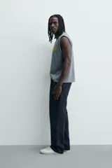 Musculosa de corte relajado con efecto lavado, cuello redondo y sisas amplias. Presenta estampados gráficos en color amarillo en el frente y acabados irregulares que le otorgan una apariencia única.