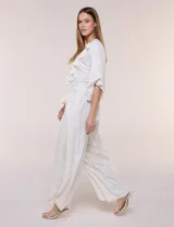 Blusa blanca de silueta holgada con sutil trama en hilo metalizado lurex, escote en V con pechera tejida en crochet y apliques de borlas en el contorno del cuello y las mangas.