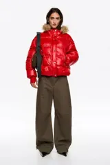 Chaqueta acolchada corta de tejido técnico brillante en color rojo, con cierre frontal de cremallera y botones de presión. Presenta capucha con borde de pelo sintético desmontable, bolsillos laterales con cremallera y puños de punto elástico en color rojo.