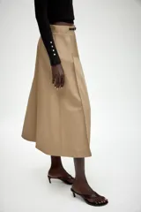 Falda midi de tiro alto en color beige, con diseño evasé y pliegues laterales. Incluye un cinturón fino a contraste en color negro con hebilla metálica y cierre frontal con cremallera y gancho.