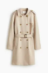 Gabardina de color beige claro, largo hasta la rodilla, de doble botonadura con botones marrones. Presenta solapas clásicas, hombreras, cinturón de tela extraíble con hebilla oscura y bolsillos insertados.