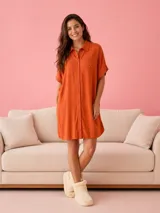 Camisa tipo vestido de corte holgado, confeccionada en viscosa suave, con cuello camisero, cierre frontal de botones, mangas cortas con dobladillo y bolsillos laterales. Presenta un pequeño bordado de corazón en el pecho.