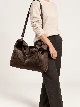 Cartera de cuero graneado marrón, de diseño amplio y desestructurado, con asas cortas para mano y correa larga regulable para hombro.