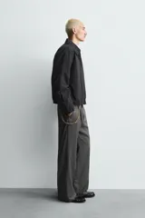 Cazadora de hombre de ajuste cropped fit, confeccionada en tejido de algodón con patrón de rayas verticales finas en tonos oscuros (negro/azul marino y marrón/beige). Presenta cuello solapa, cierre frontal de cremallera, bolsillos laterales y elástico en puños y bajo.