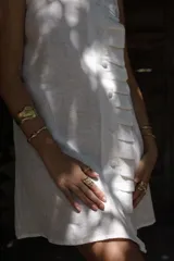 Vestido corto de lino sin mangas, con cuello alto adornado con un volado. Presenta un acceso frontal cruzado con botones forrados en la misma tela y un largo por encima de la rodilla.