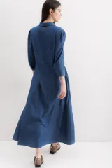 Vestido camisero largo de denim azul, con cuello clásico, mangas 3/4 abullonadas y falda amplia con bolsillos laterales.