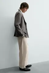 Pantalón chino de corte relajado, confeccionado en tejido estructurado de color beige. Presenta bolsillos frontales, bolsillos traseros de vivo y cierre frontal con cremallera y botón.