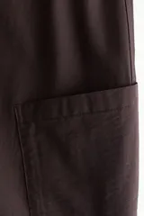 Pantalón cargo de corte holgado en color marrón, confeccionado en mezcla de algodón y nailon. Presenta cintura elástica de talle alto y perneras estilo globo con bolsillos tipo parche a los lados y costuras visibles en la parte delantera.