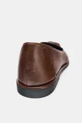 Mocasín de cuero color marrón con detalle de borlas en el empeine y perforaciones decorativas tipo brogue en la puntera y el talón.
