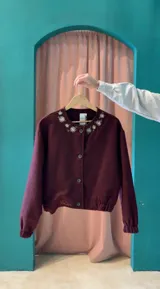 Campera bomber bordada color bordó, confeccionada en paño de lana, con cuello redondo, cierre frontal de botones y detalles elásticos en los puños y el ruedo.