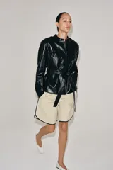 Cazadora efecto piel de Zara Woman Collection, en color negro. Cuenta con cuello redondo, manga larga, bolsillos de parche con solapa en el delantero y cierre frontal con botones forrados. Incluye un cinturón del mismo tejido para ajustar en la cintura.