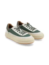 Sneaker de diseño urbano con combinación de texturas y colores, presentando paneles en verde oscuro y cuero texturizado en tono crudo, con suela de plataforma en color crema y base de goma.
