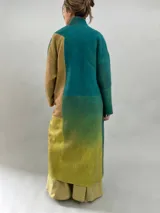 Tapado largo de lana merino afieltrada con diseño de paneles en degradé de tonos verdes y ocres. Presenta hombros caídos, mangas rectas, bolsillos laterales y cierre frontal con broches ocultos.