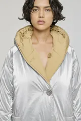 Campera reversible de corte regular, confeccionada en nylon con acabado repelente al agua. Presenta diseño con capucha, mangas raglán y cierre frontal con botones. Un lado es de color negro con bolsillos de parche, mientras que el reverso es de color plateado con bolsillos laterales integrados.