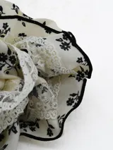 Colita para el pelo tipo scrunchie de tela color crema con estampado floral negro y borde con terminación en hilo negro.