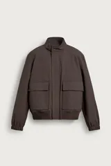 Cazadora regular fit de tejido técnico color marrón, con cuello subido, cierre frontal con cremallera oculta y solapa con botones a presión. Cuenta con bolsillos de plastrón con solapa en la cadera y acabados en rib elástico en puños y cintura. Incluye un chaleco interior acolchado desmontable.