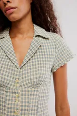 Camisa de mezcla de algodón y lino, de cuerpo entallado, con diseño a cuadros en tonos verde y beige. Presenta escote en V con cuello de solapa, mangas cortas y cierre frontal con botones.