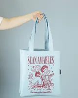 Tote bag de color celeste con estampado frontal en color bordó que incluye la frase 'Sean Amables' y dibujos de personajes infantiles en monopatines.