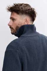 Sweater de punto acanalado en color marrón oscuro, con cuello alto y cierre frontal de cremallera parcial. Presenta mangas largas y puños ajustados.