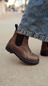 Bota Chelsea de cuero marrón con elásticos laterales negros, tiradores traseros y suela track negra.