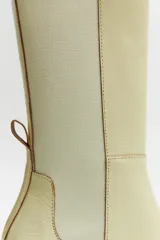 Botas de cuero color crema, de media caña, con paneles laterales elásticos, punta cuadrada y taco geométrico.