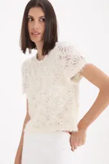 Sweater de punto de textura suave en color crudo, con diseño de flores bordadas y lentejuelas aplicadas. Presenta cuello redondo y mangas cortas, con un corte recto y holgado.