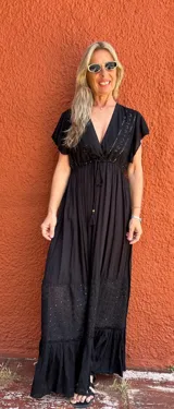 Vestido largo negro con escote en V, mangas cortas con volados, corte imperio con lazo ajustable y falda escalonada con detalles bordados.