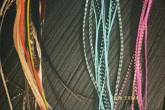 Conjunto de extensiones de plumas y tiras de cabello sintético en varios colores: tonos naturales (beige, marrón, naranja, amarillo), turquesa con patrones moteados, y rosa vibrante.