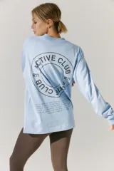 Remerón de manga larga color celeste, con cuello redondo y puños acanalados. Presenta una estampa circular en la espalda con el texto 'ACTIVE CLUB' y detalles de texto adicional en la parte inferior.