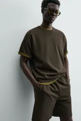 Sudadera de manga corta con cuello redondo, confeccionada en tejido texturizado de color verde oscuro/marrón. Presenta un corte relajado (relaxed fit).