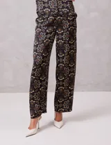 Conjunto de dos piezas compuesto por una blusa sin mangas con cuello solapa y escote en V con botones frontales, y un pantalón de tiro alto con pierna ancha y bolsillos laterales. Ambas prendas están confeccionadas en satén con un estampado floral sobre fondo oscuro.