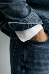 Cazadora de denim de algodón, color azul medio lavado, con cuello solapa, manga larga y cierre frontal de botonadura. Presenta cuatro bolsillos de plastrón con tapa y botón en el frente (dos en el pecho y dos a la altura de la cadera).