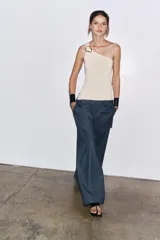 Top blanco de punto con escote asimétrico y aplique metálico dorado en el hombro.