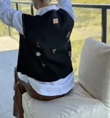 Chaleco negro con cierre frontal de botones, decorado con flores bordadas a mano y costuras decorativas en los bordes.