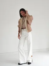 Pantalón vaquero de tiro alto y corte recto, color blanco, con aberturas laterales en los bajos y detalles de terminación en cuero.