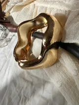 Brazalete rígido de diseño orgánico y ondulado, con acabado metálico plateado de alto brillo.