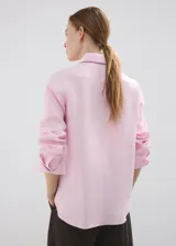 Camisa de lino color rosado, con diseño recto, cuello camisero, manga larga con puños abotonados y cierre frontal de botones.