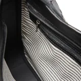 Cartera tipo bandolera de cuero negro con textura granulada. Presenta una correa ancha ajustable con detalles de ojales metálicos y un aplique metálico con el logo de la marca en la parte frontal.