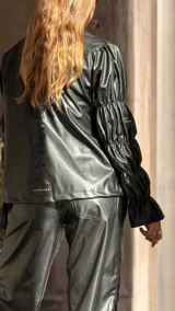 Camisa de cuero sintético color negro, con cuello redondo, cierre frontal con botones y mangas largas con diseño fruncido y volados en los puños.