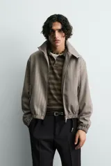 Cazadora cropped de hombre con tejido de estructura espiga. Presenta cuello subido con cierre de botones, cierre frontal de cremallera, bolsillos laterales con solapa y acabados elásticos en puños y cintura.