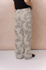 Jean wide leg de tiro alto con estampado floral integral en tonos grises sobre base beige. Cuenta con cierre frontal con botón, pasacintos y bolsillos funcionales delanteros y traseros.