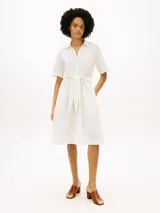 Vestido midi color blanco de Tommy Hilfiger, confeccionado en lino y algodón. Presenta cuello camisero, manga corta, cierre frontal oculto y un cinturón ajustable anudado en la cintura. La falda tiene diseño acampanado y largo por debajo de la rodilla.
