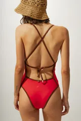 Malla enteriza de color rojo con breteles finos y bordes en contraste color marrón. Presenta un escote en V profundo y un corte de pierna alto.