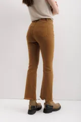 Pantalón de jean color marrón óxido, tiro medio, corte ajustado en muslos y ligeramente acampanado en la parte inferior (bootcut/flare), con bajo desflecado.
