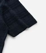 Remera tipo polo de manga corta con cuello en V, confeccionada en un tejido con textura patchwork. Presenta un diseño elegante y versátil, ideal para un look casual o formal.