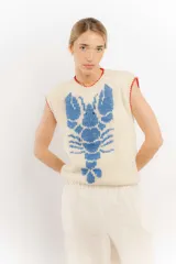 Chaleco tejido a mano en lana merino, color beige con diseño de langosta en color azul y detalles de terminación en rojo en cuello y sisas.