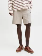 Bermuda deportiva beige de calce relajado, con costuras frontales en relieve y pequeño estampado lateral.