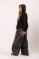 Pantalón de jean negro con proceso de lavado localizado, corte balloon fit de volumen curvo, detalles de bordados tipo costura expuesta y parches desflecados.
