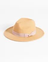 Sombrero tipo fedora de fieltro color beige claro, con ala ancha y copa pinchada. Presenta una cinta de tela de color rosado pálido anudada alrededor de la base de la copa.